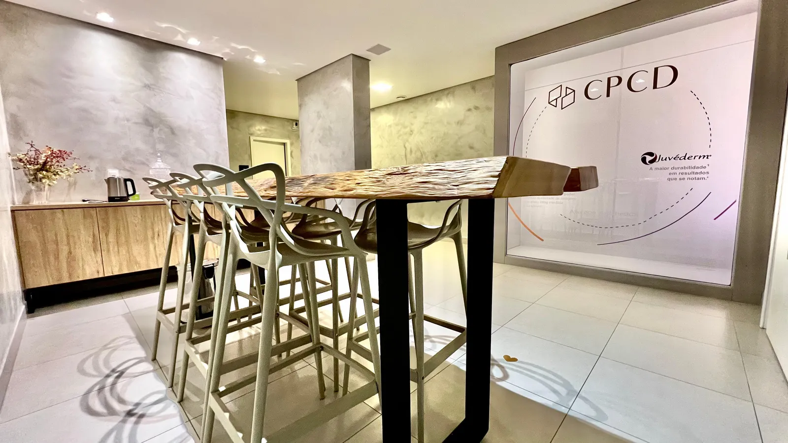 Espaço de convivência do CPCD com mesa alta, banquetas e painel com a marca